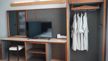 Une chambre d’hôtel équipée d’un bureau en bois, d’une télévision, d’une chaise, d’une armoire et d’un porte-vêtements.