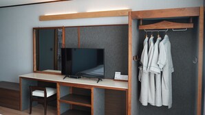Ein modernes Hotelzimmer mit einem Holztisch, einem Fernseher, einer Sitzecke und einem Kleiderständer für Bademäntel.