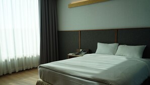 Ein Hotelzimmer mit einem großen Bett, einem Nachttisch mit Telefon und einem Fenster mit Vorhängen.