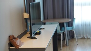 Ein Hotelzimmer mit Schreibtisch, Stuhl, Computer und brauner Tasche auf dem Schreibtisch.