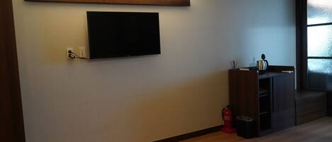 Una sala de estar moderna con un televisor de pantalla plana montado en la pared, piso de madera y un mueble empotrado con una tetera.