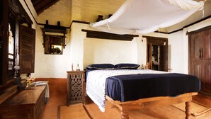 Une chambre traditionnelle avec un lit en bois, une table de chevet, un baldaquin blanc suspendu et une décoration rustique.