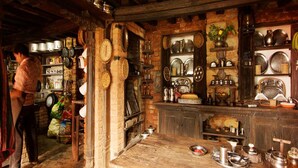 Une cuisine rustique avec des poutres en bois, des étagères remplies d’ustensiles de cuisine et une table en bois sur laquelle sont disposés de la vaisselle.