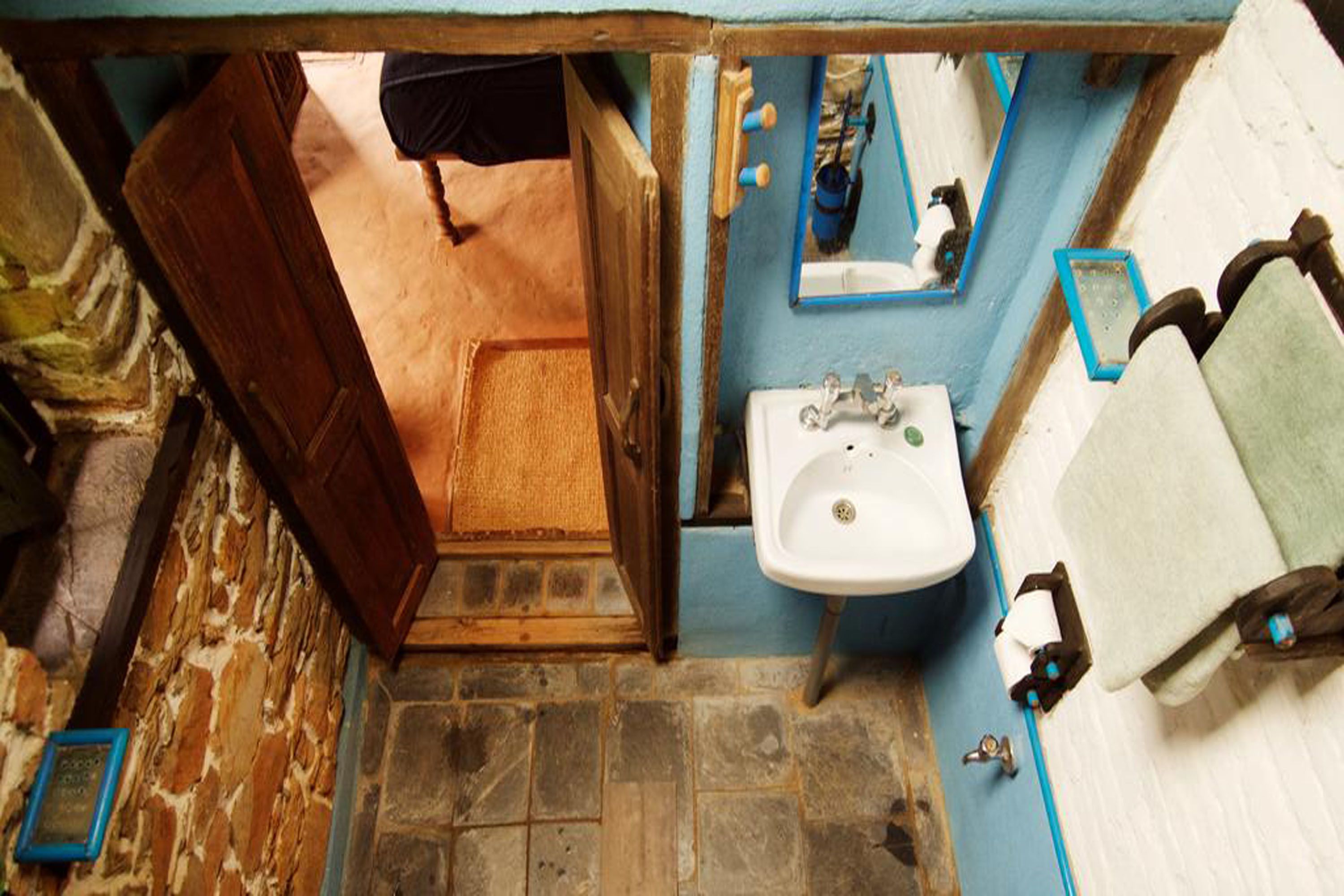 Un baño estrecho con piso de piedra, un lavamanos blanco y un espejo encima.