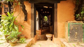 Une entrée avec un chemin de pierre menant à une porte en bois, bordée de plantes en pot et surmontée d’une façade de bâtiment au style rustique.