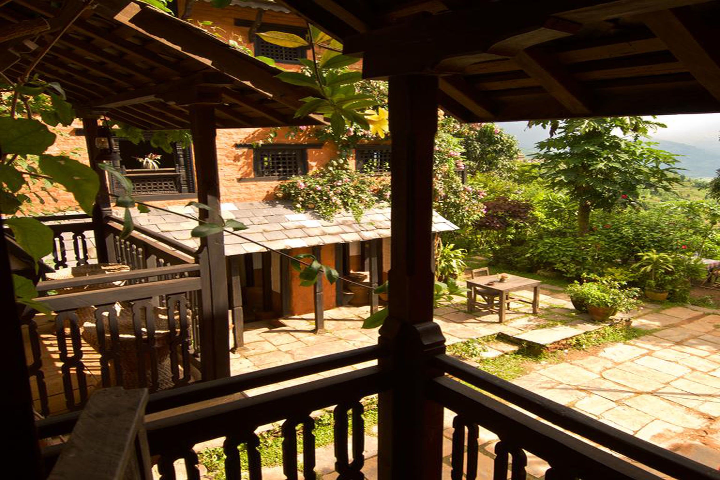 Un espacio al aire libre cubierto con una pérgola de madera, suelo de piedra y vistas a un edificio con techo de tejas.