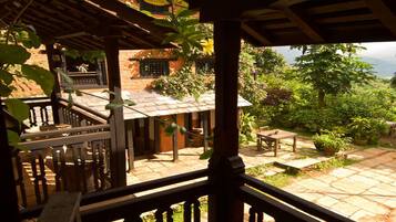 Un espacio al aire libre cubierto con una pérgola de madera, suelo de piedra y vistas a un edificio con techo de tejas.