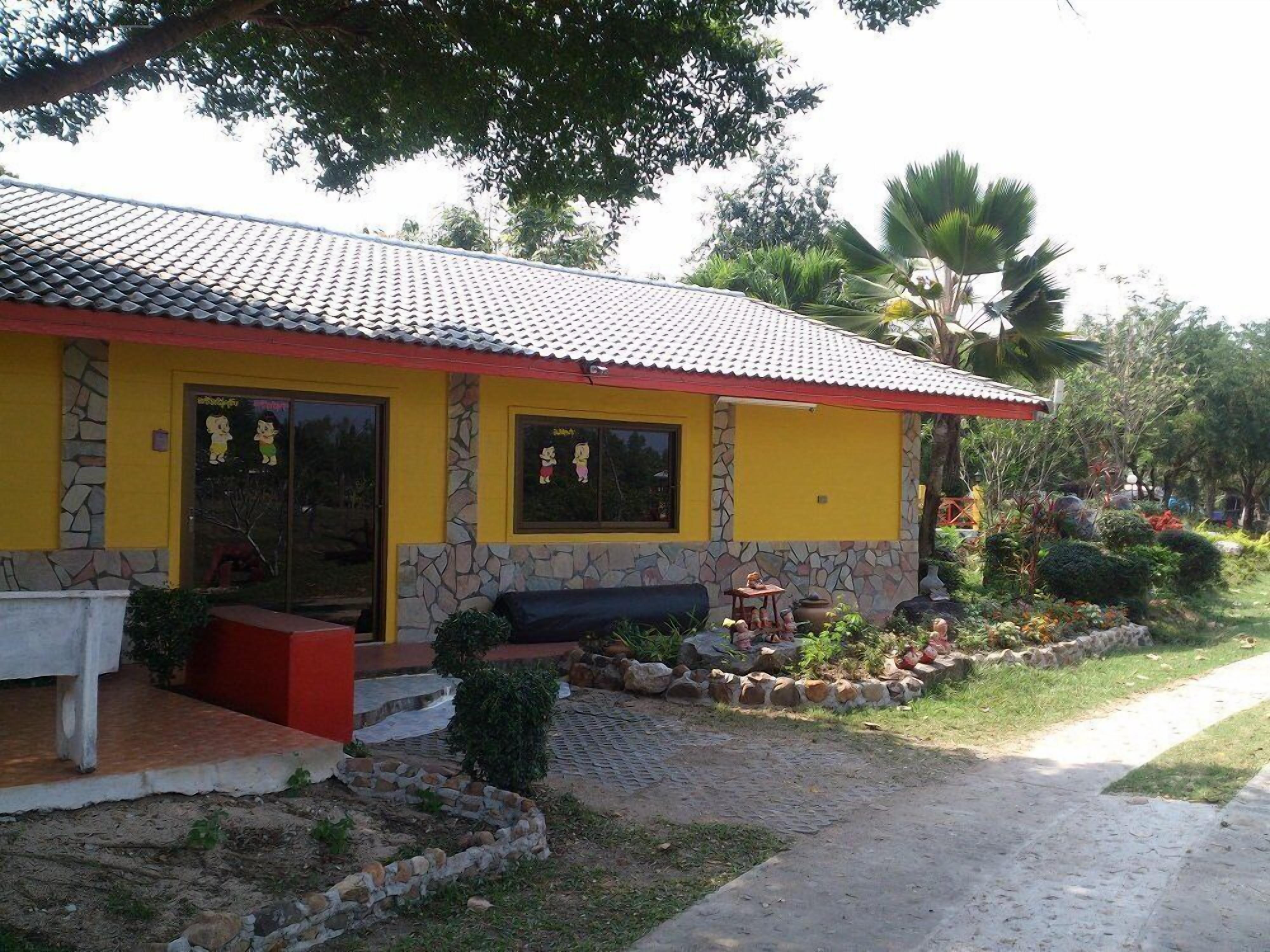 Um edifício amarelo com telhado ladrilhado, paredes de pedra e um pequeno alpendre com um banco.