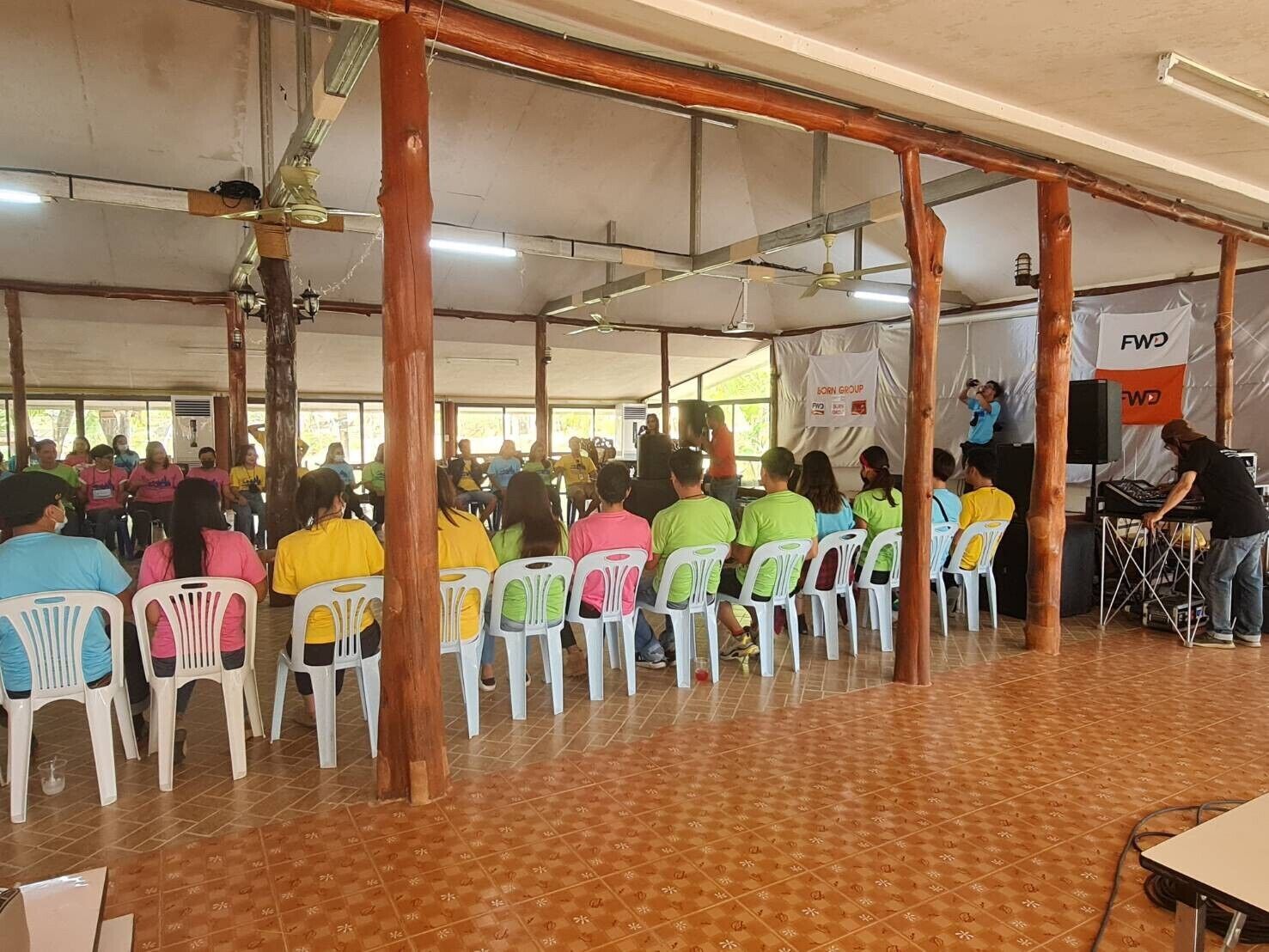A covered indoor space with rows of plastic chairs and a stage area with a banner.