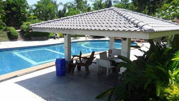 A covered pool area with a tiled roof, a lounge chair, and a table.