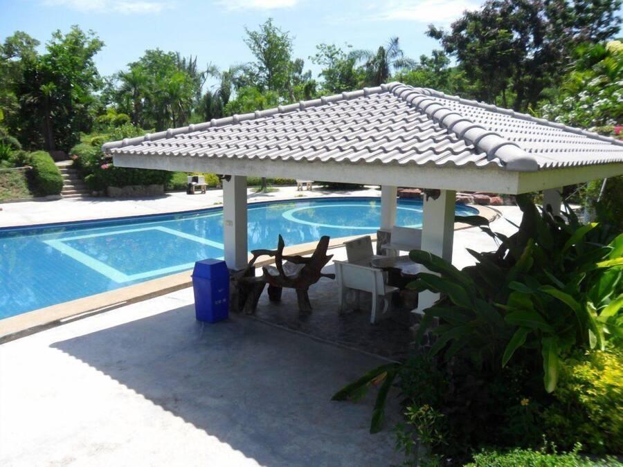 A covered pool area with a tiled roof, a lounge chair, and a table.