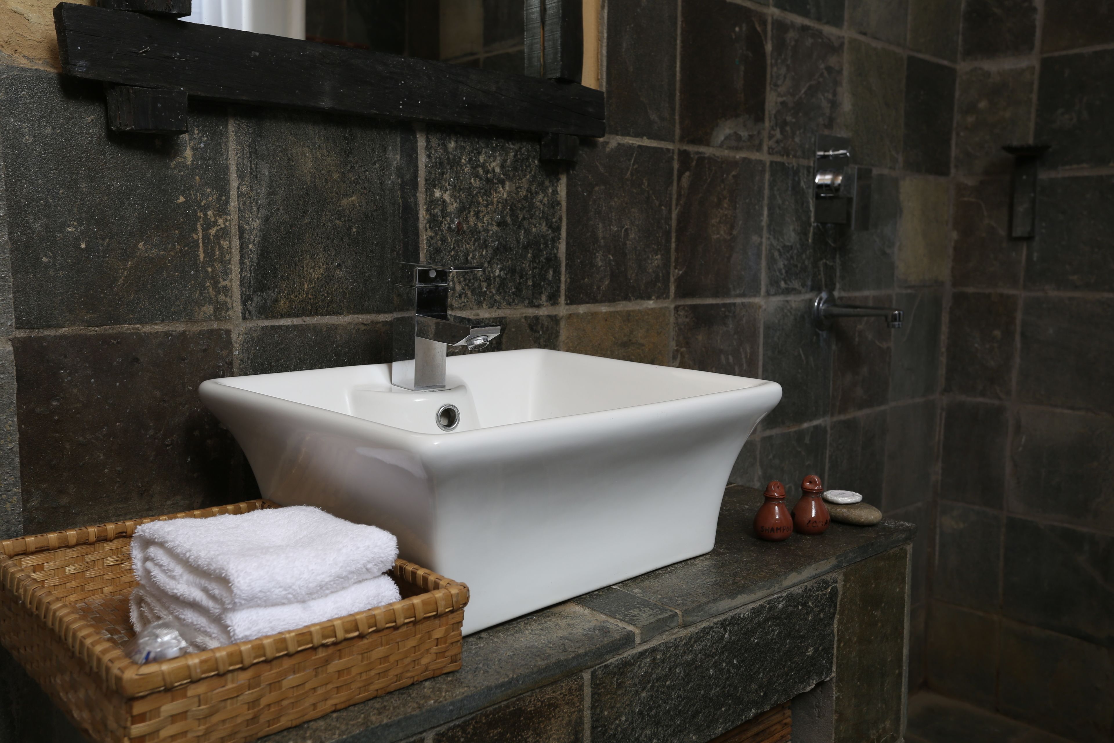 Un baño con un lavabo blanco, una cesta de madera con toallas y una pared de piedra.