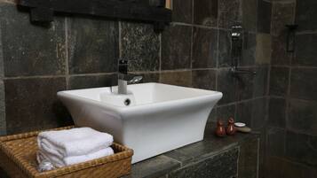 Un baño con un lavabo blanco, una cesta de madera con toallas y una pared de piedra.