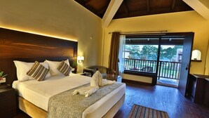 Una habitación de hotel con una cama grande, techo de madera, balcón con vistas y una mesita de noche con lámpara.