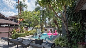 A pool area with lounge chairs, a swimming pool, and tropical plants.