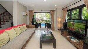 A living room with a sofa, coffee table, TV, and a view of a pool and garden.