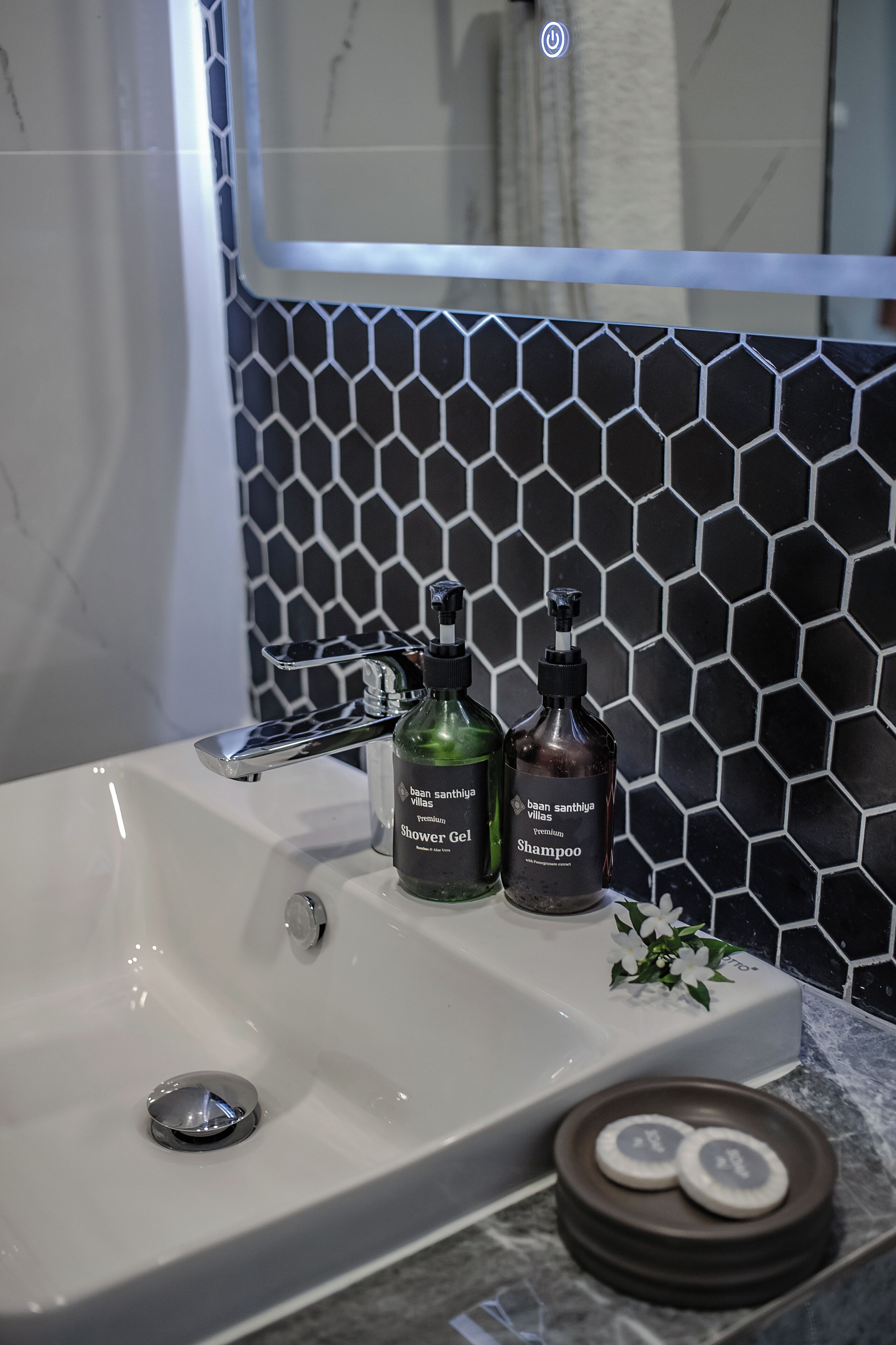 A bathroom with a white sink, two bottles of shower gel and shampoo, and a mirror above the sink.
