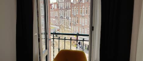 A room with a yellow armchair, a glass table, and a view of a cityscape through a large window with black curtains.