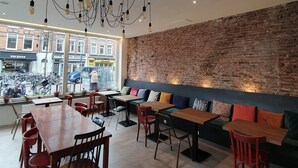 A cafe with a brick wall, wooden tables, and chairs. - Hotel Heye 130 (Amsterdam)