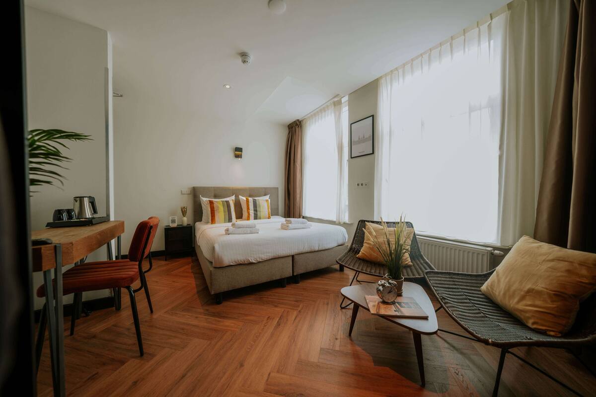 A hotel room with a bed, a desk, a chair, a sofa, and a window with curtains.