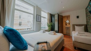 A hotel room with a large bed, a sitting area with a chair, a small table, and a view of buildings outside the window. - Hotel Heye 130 (Amsterdam)