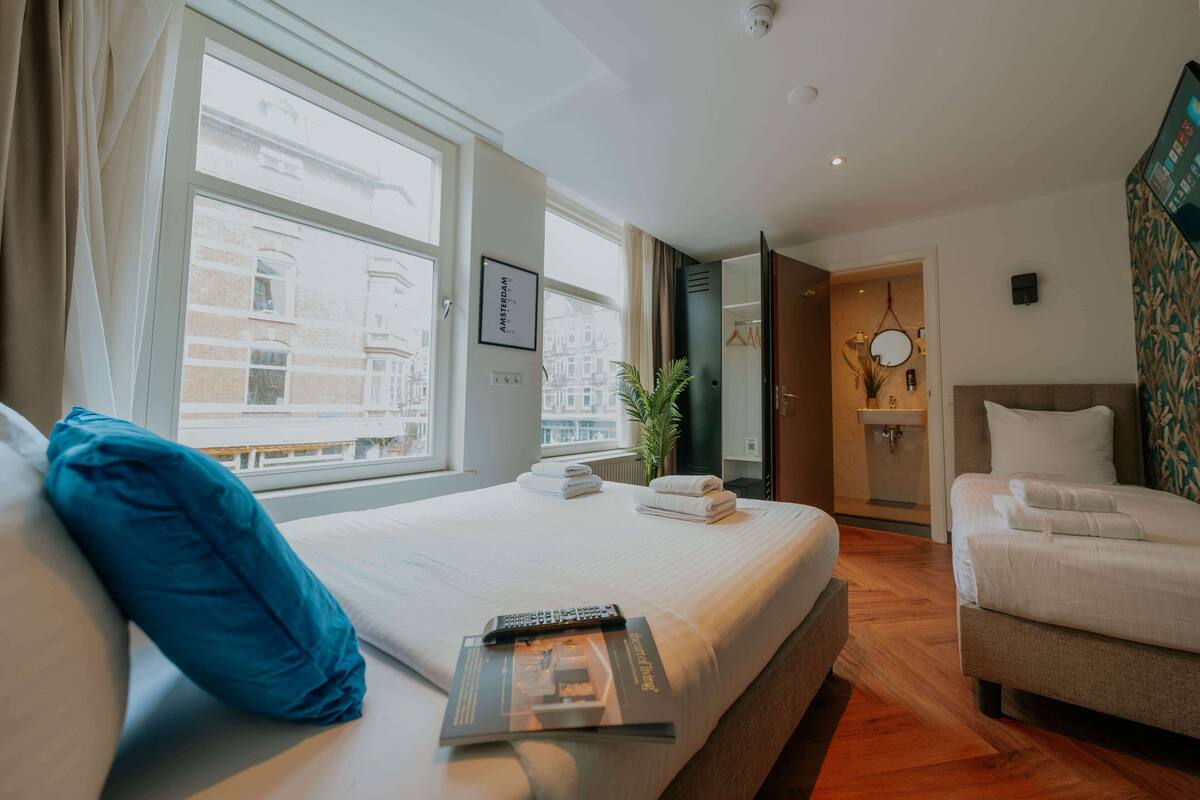 A hotel room with a large bed, a sitting area with a chair, a small table, and a view of buildings outside the window.