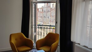 A room with two yellow chairs, a small table, and a view of a cityscape through a window with black curtains. - Hotel Heye 130 (Amsterdam)