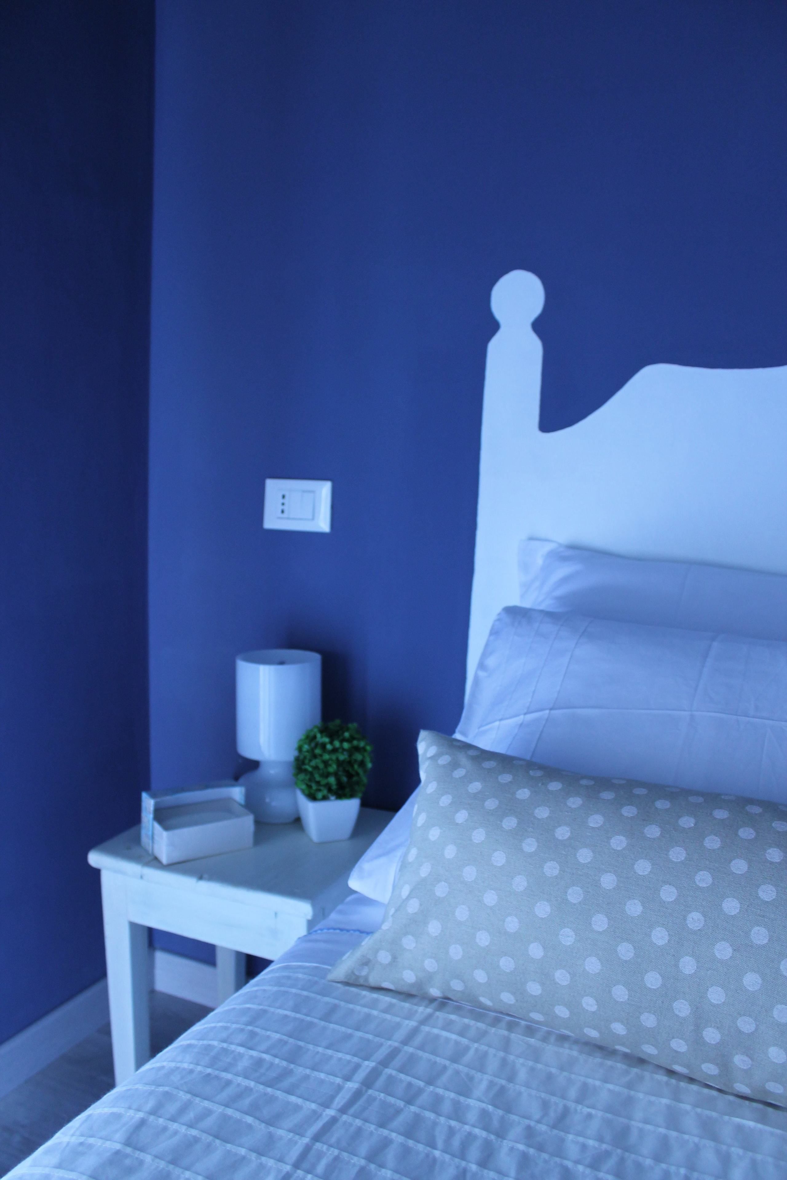 A neatly made bed with white bedding and a grey pillow with white polka dots.