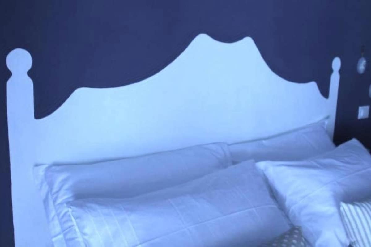 A white bed with a headboard against a dark wall.