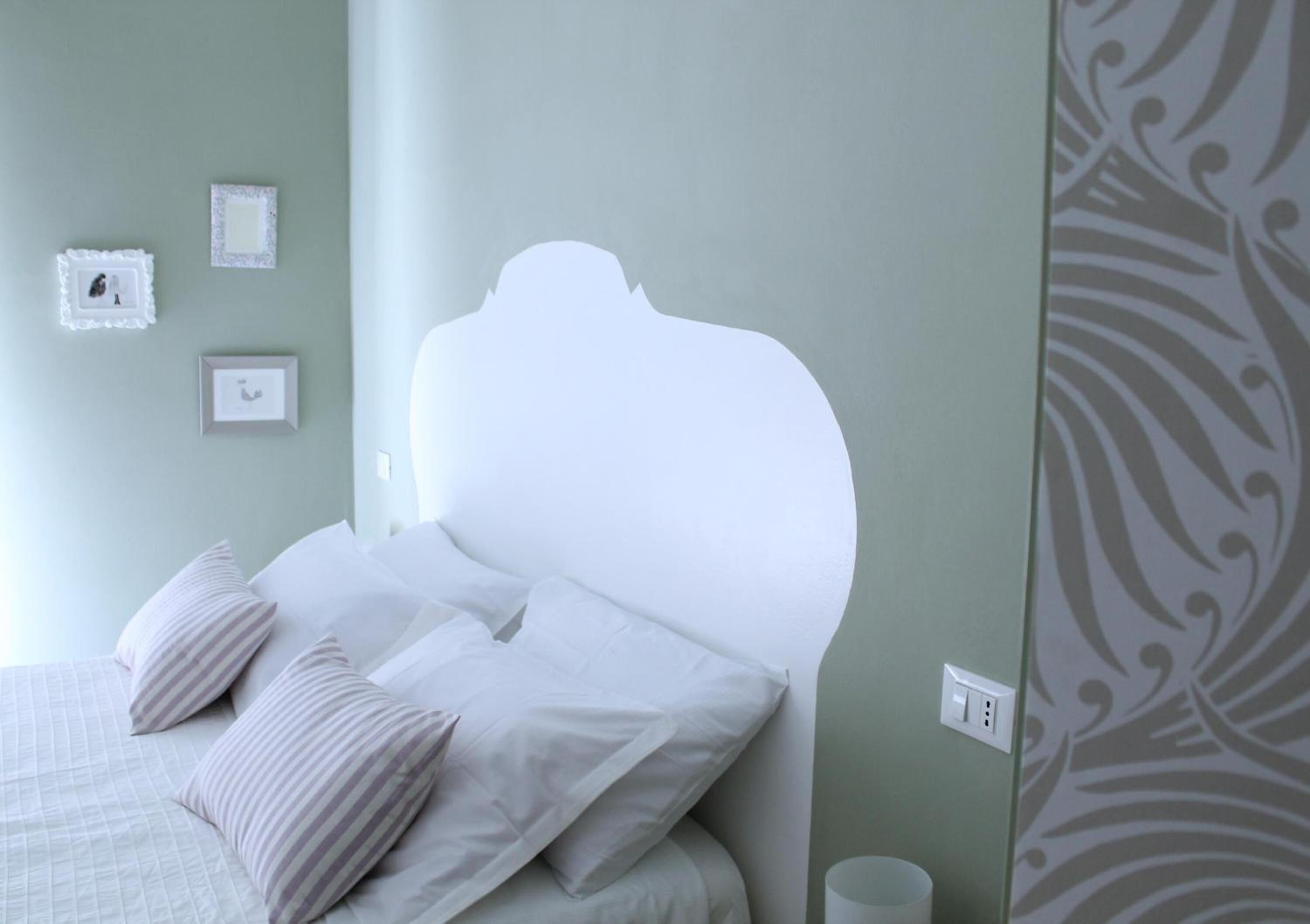 A neatly made bed with white bedding and striped pillows, a wall with three framed pictures, and a patterned curtain.