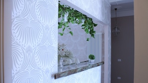 Een kamer met behang met patroon, een houten plank met decoratieve objecten, en een hangplant.