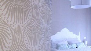 Een slaapkamer met behang met een patroon, een bed met een witte hoofdeinde en een hanglamp.