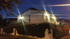 Een tweelaags huis met een balkon, omgeven door groen en een witte hek.