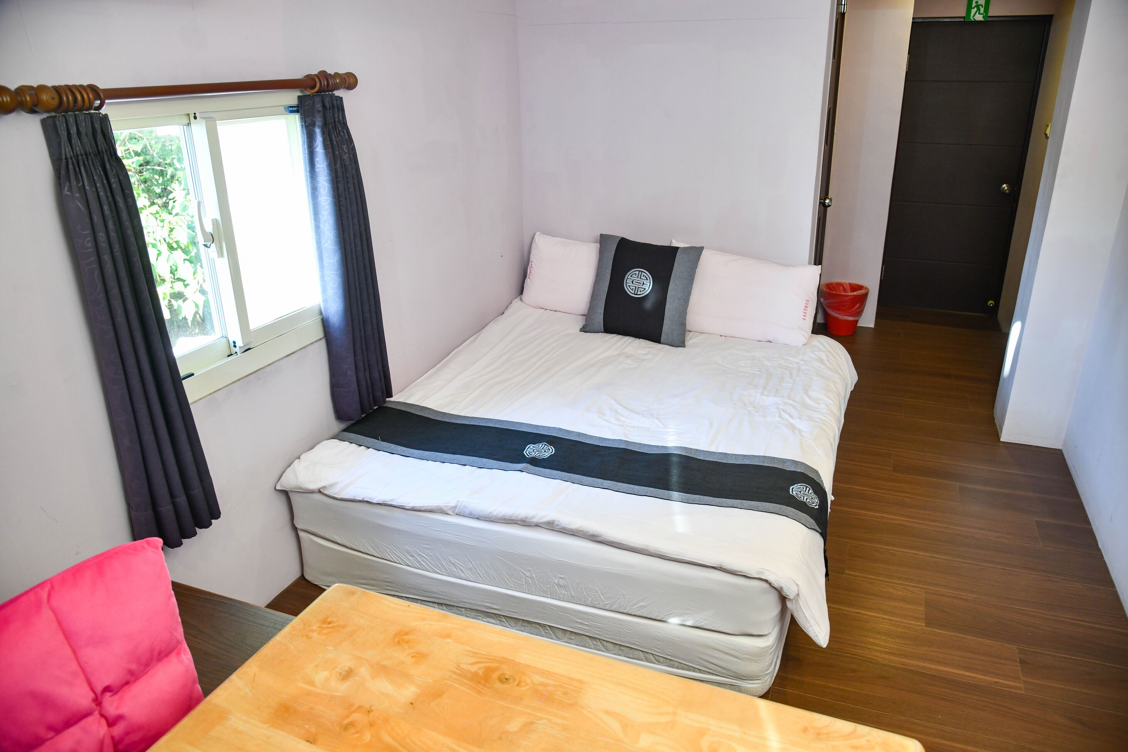A neatly arranged bedroom with a bed, a wooden table, and a red chair.