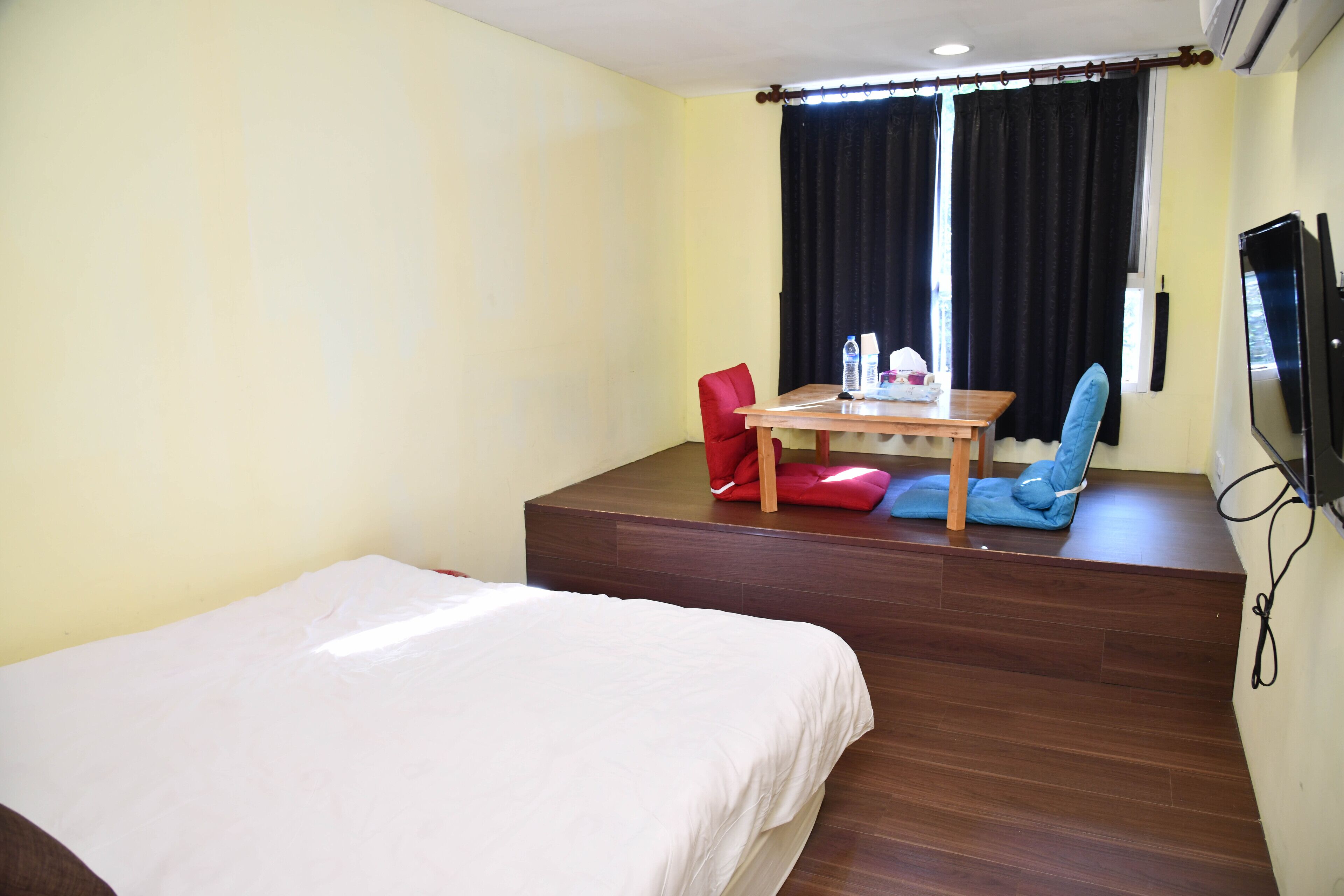 A hotel room with a bed, a table with chairs, a TV, and a window with curtains.