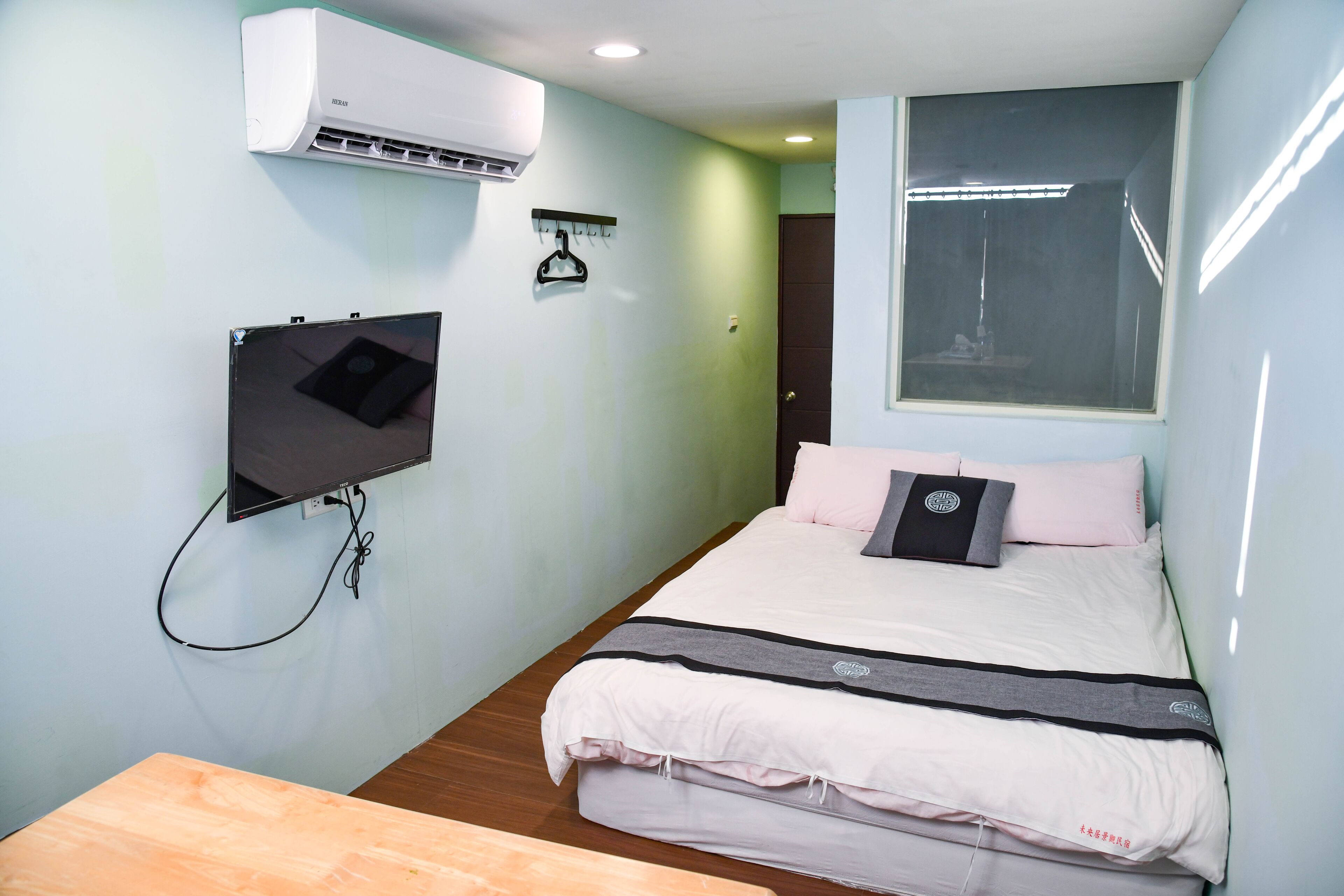 A bedroom with a bed, a TV mounted on the wall, an air conditioner, and a window.