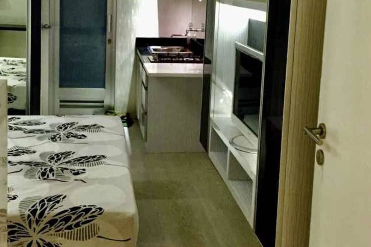 A narrow room with a bed, a kitchenette, and a television.