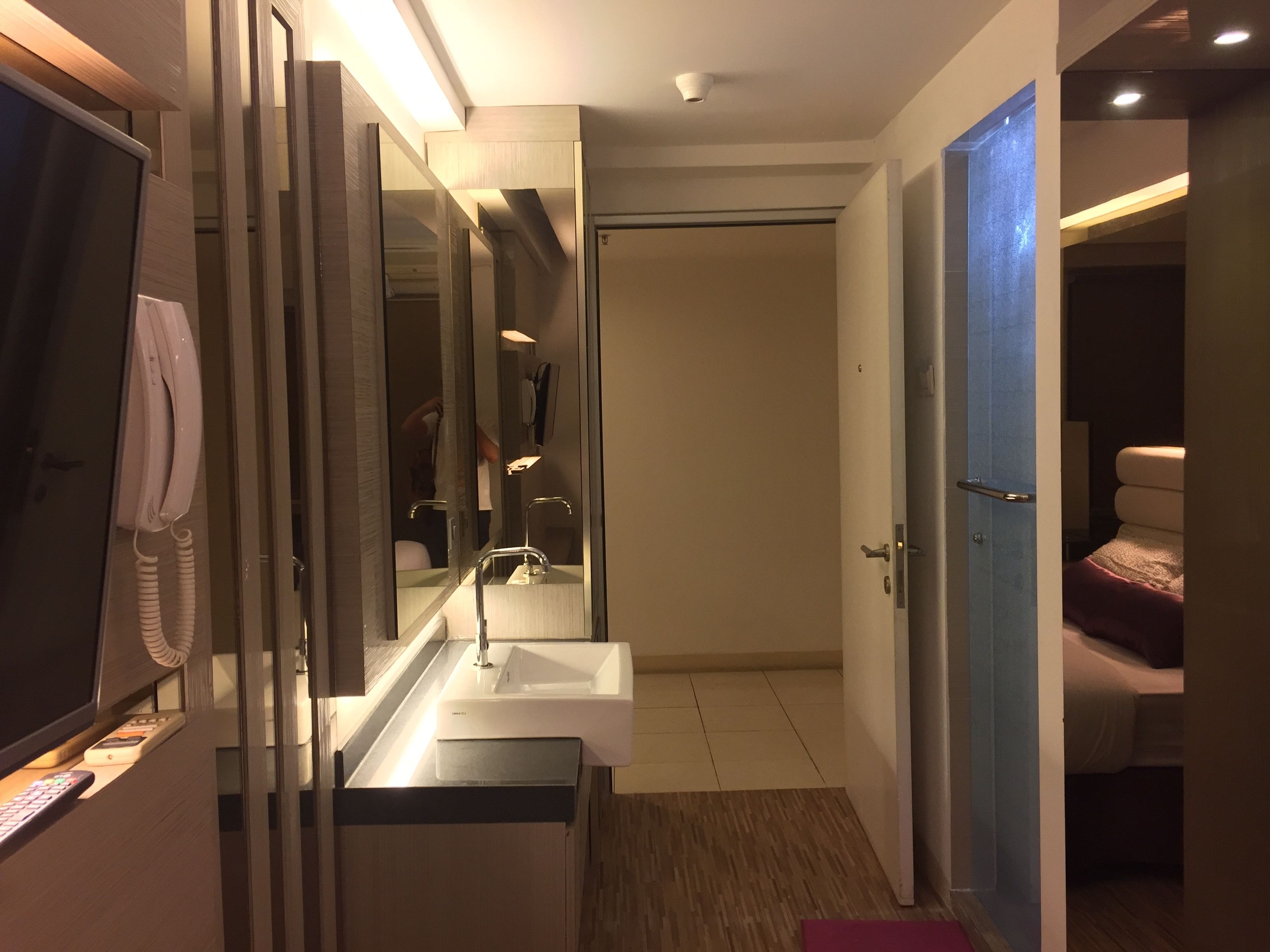 Een moderne badkamer met een grote spiegel, een wastafel en een toilet, zichtbaar door een open deur.