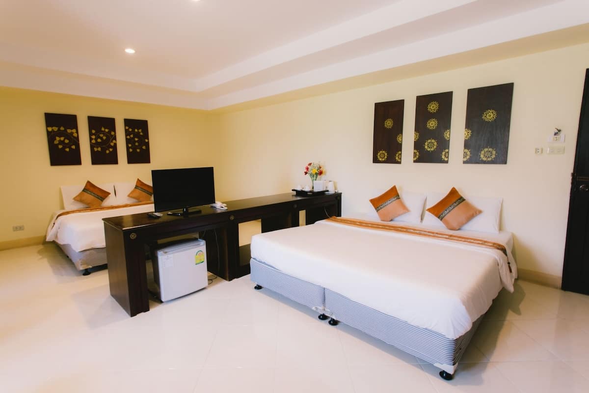 A hotel room with two beds, a desk, a TV, and a small refrigerator.