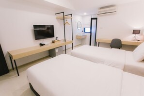 A hotel room with two beds, a desk, a TV, a mirror, and a small desk lamp.
