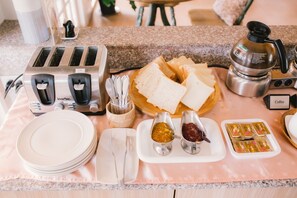 A breakfast setup with a toaster, two slices of bread, a coffee maker, and condiments on a countertop.