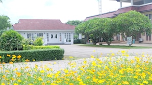 A building with a red-tiled roof, surrounded by a well-maintained garden with yellow flowers. - Royal Princess City (Lamphun)