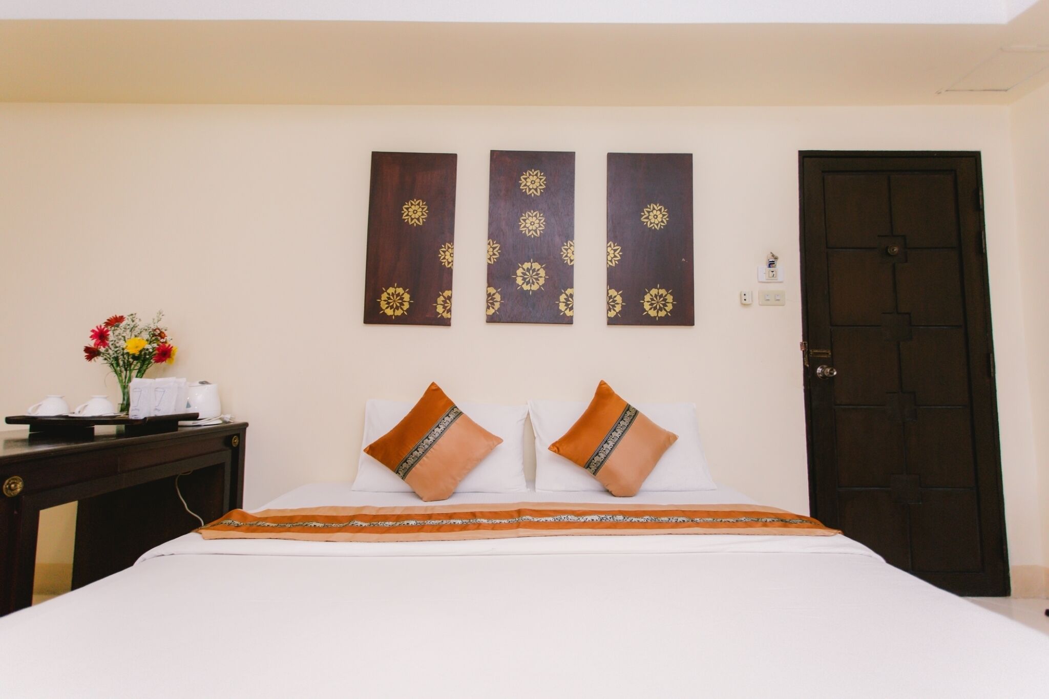 A hotel room with a bed, two pillows, a nightstand with a vase of flowers, and three wall-mounted decorations.