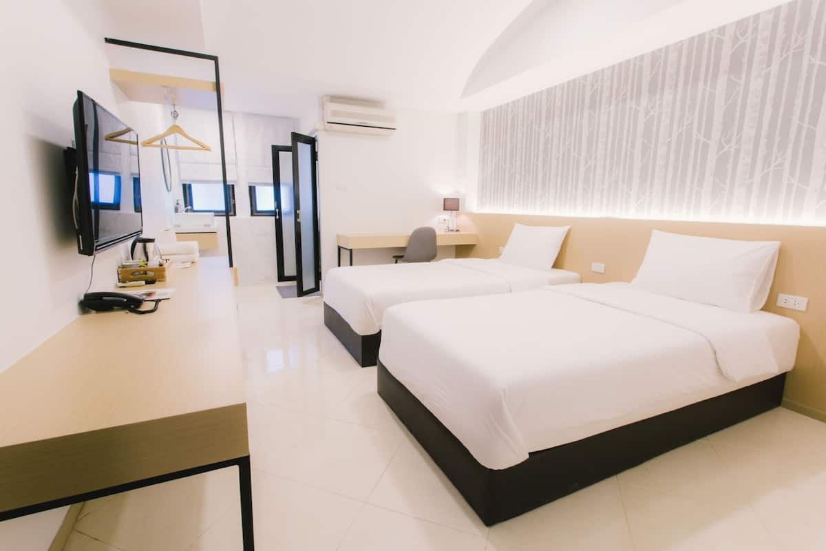 A modern hotel room with two beds, a desk, a TV, and a mirror.