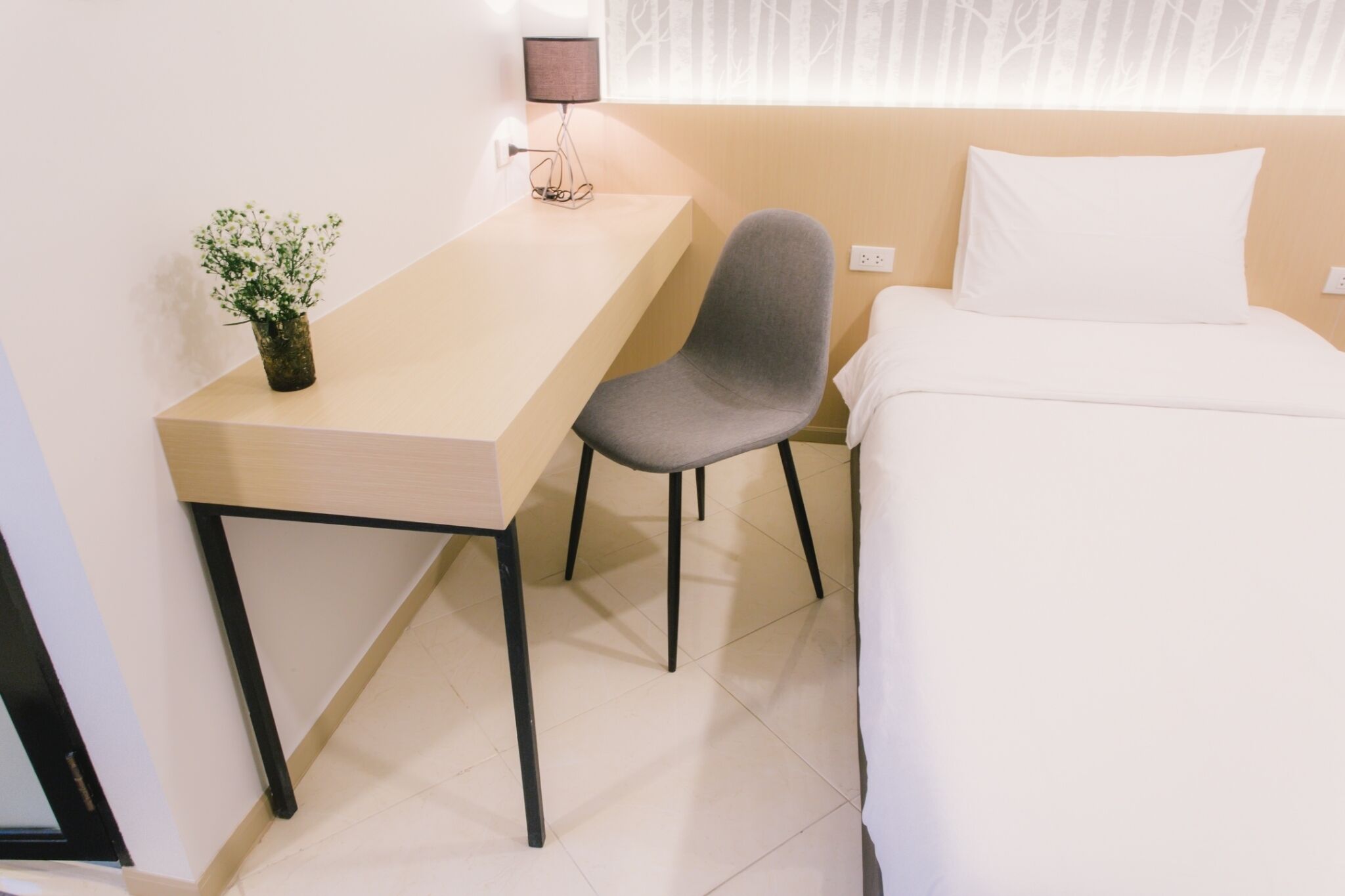 A compact hotel room with a single bed, a small desk, and a chair.