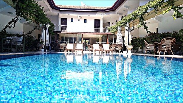 A swimming pool with lounge chairs and umbrellas, surrounded by a building with a balcony and potted plants. - Eon Dalyan Boutique Hotel (Ortaca)