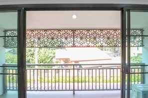 A balcony with a metal railing, a decorative patterned divider, and a view of a building with a red roof. - Baan Hauen Inn (Chiang Mai)