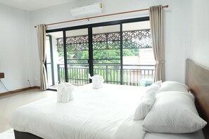 A hotel room with a large bed, white linens, a view through a window with a decorative screen, and a balcony with a railing. - Baan Hauen Inn (Chiang Mai)