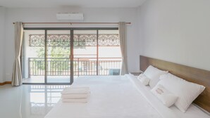 A hotel room with a large bed, a balcony with a view, and an air conditioning unit. - Baan Hauen Inn (Chiang Mai)