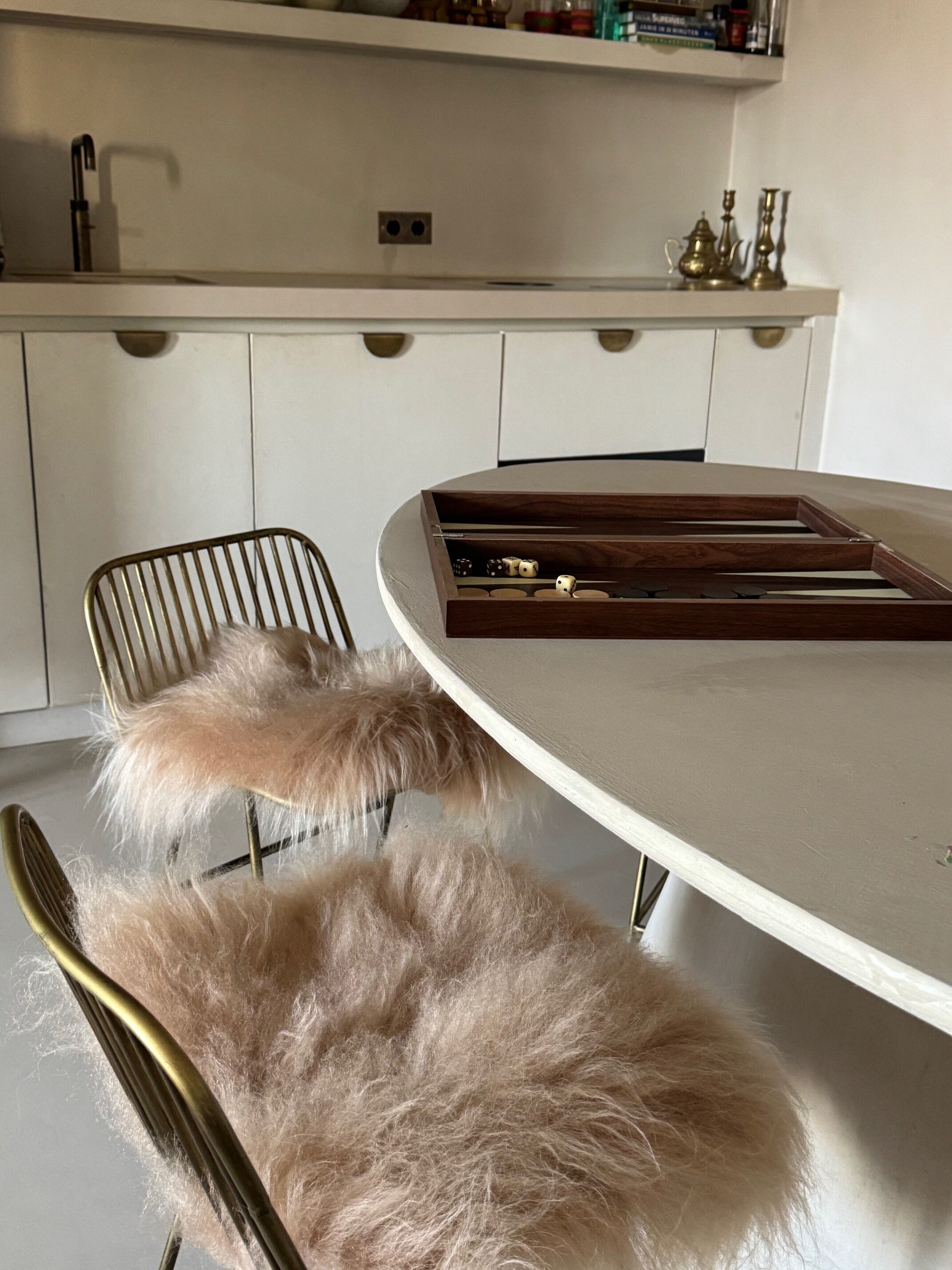 A modern kitchen with white cabinets, a round dining table, and a fur-covered chair.